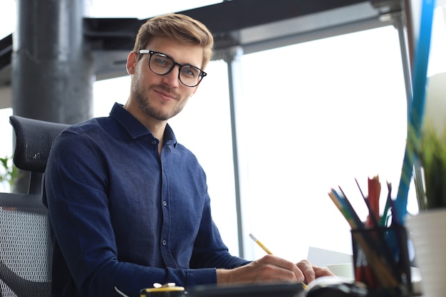 Bello giovane uomo d'affari che disegna qualcosa mentre lavora in ufficio.