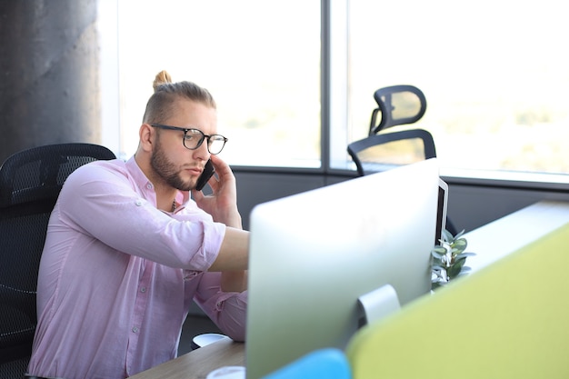 Good looking young business man talking on the smart phone while sitting in the office.