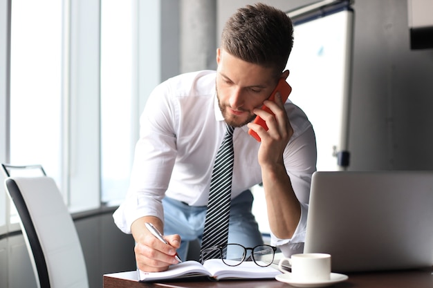 Good looking young business man talking on the smartphone while sitting in the office.