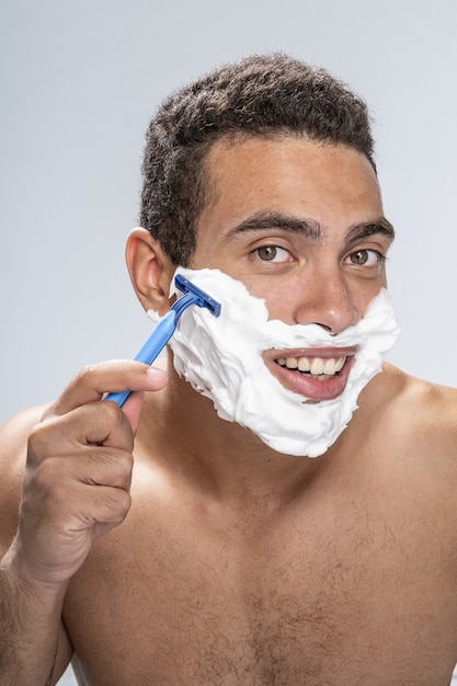 Good-looking young male smiling putting a razor to his cheek