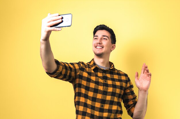 Good looking young man in casual yellow shirt video-chatting via smartphone isolated against yellow background