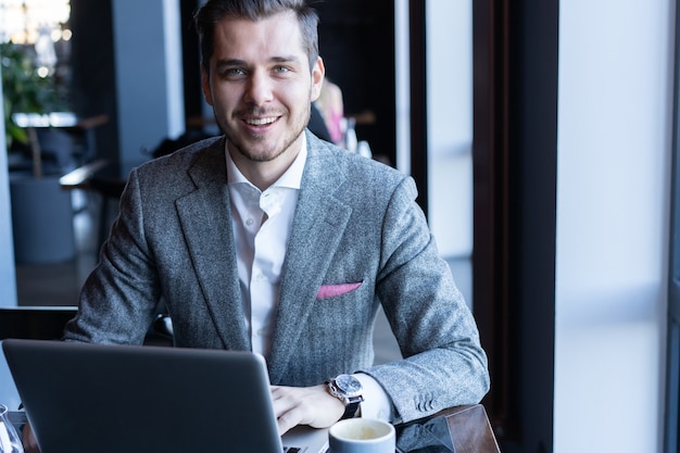 Good looking young man in full suit using computer while sitting in the cafe