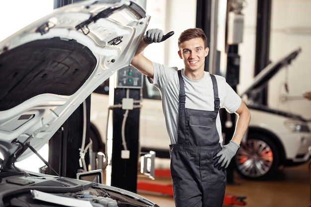 A good-looking young man is behind the car he is repairing.