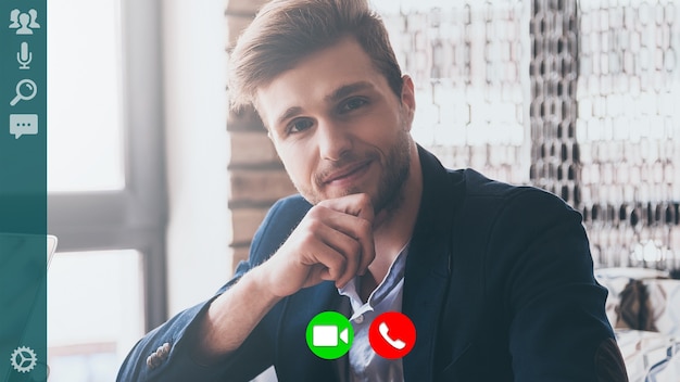 Good looking young man in smart casual wear looking at camera\
and smiling while having video call