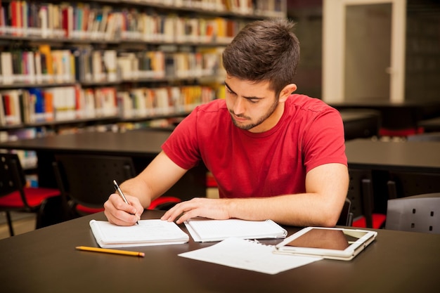 Foto giovane bello che prende alcune note e fa il lavoro di scuola in una biblioteca