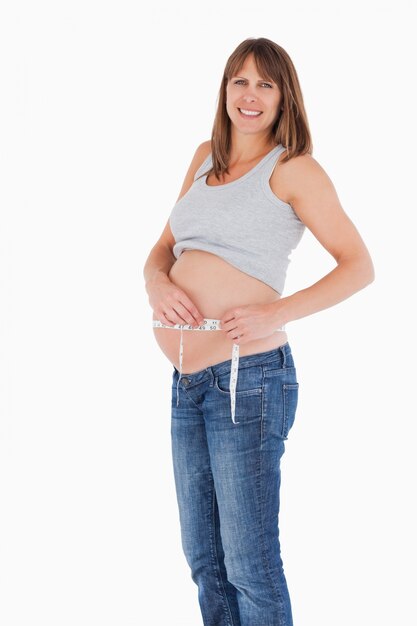 Хорошая беременная женщина, измеряющая ее живот, стоя