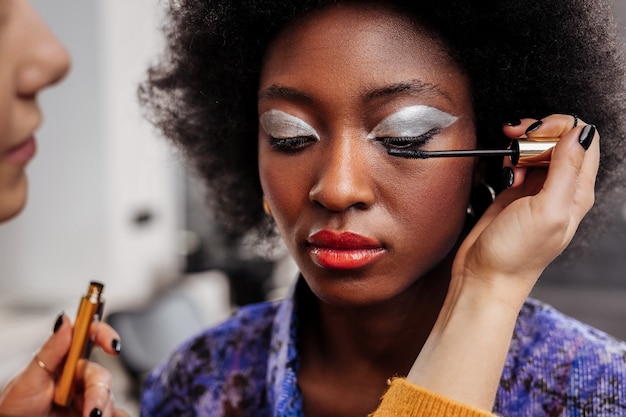 Good mood. Fair-haired young stylist with black nail polish feeling good doing makeup to a model