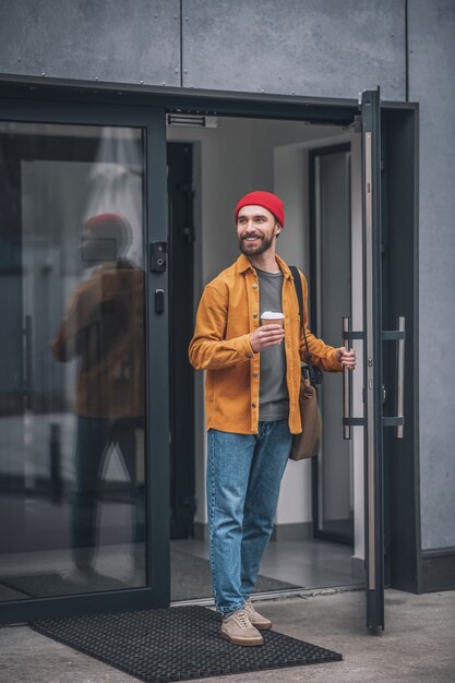 좋은 분위기. 긍정적 인 찾고 손에 커피 컵과 빨간 모자와 주황색 재킷에 남자