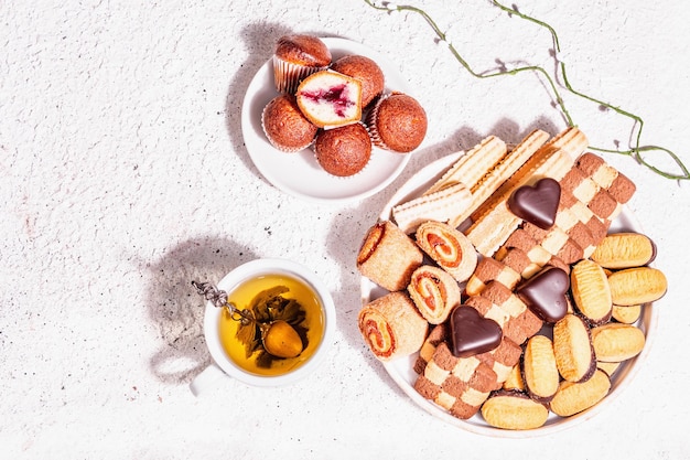 Good mood morning tea with various cookies and muffins. Fashionable hard light, dark shadow. Putty background, top view