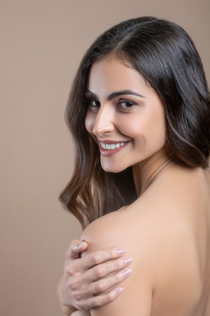 Good mood. Smiling woman with naked back holding her shoulder with her hand and turning her head