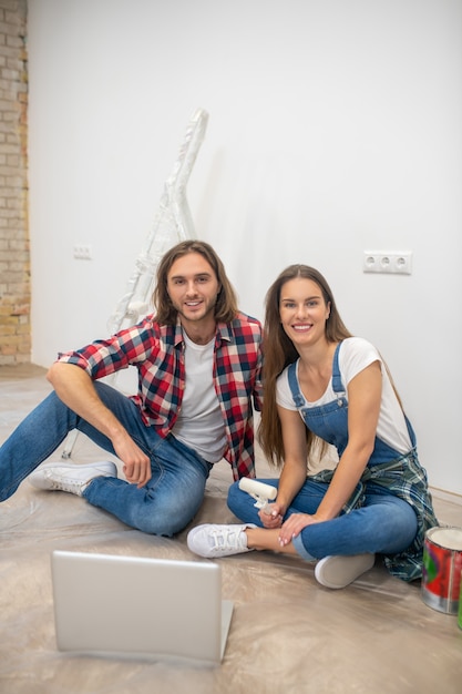 Good mood. Young couple sitting on the floor and smiling