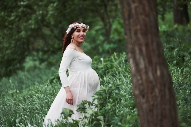 Good morning. Beautiful pregnant woman in dress have a walk outdoors. Positive brunette