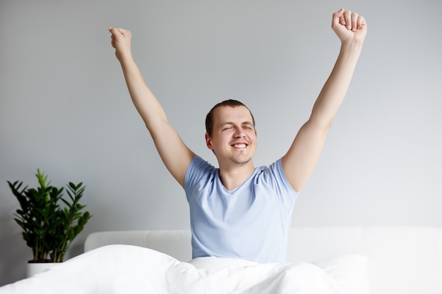 Good morning concept - portrait of young handsome man stretching in bed after sleeping