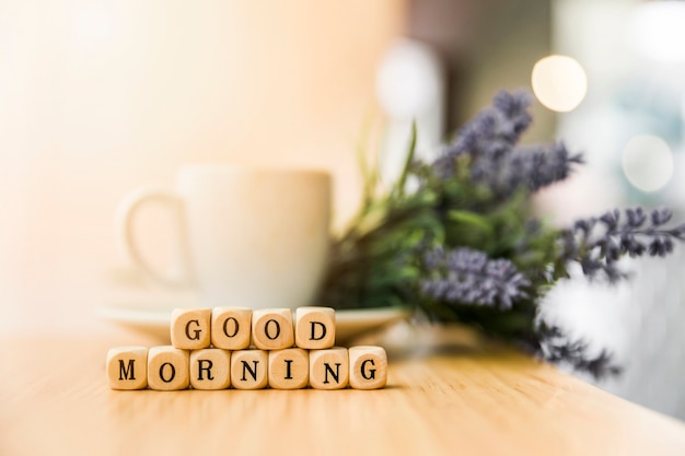 Blocchi cubici di buongiorno con la tazza di caffè e fiore sulla tavola di legno