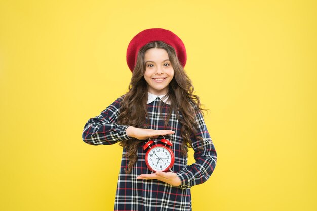 Good morning. Small child smiling in morning on yellow background. Happy little girl holding alarm clock early in the morning. Waking up in morning.