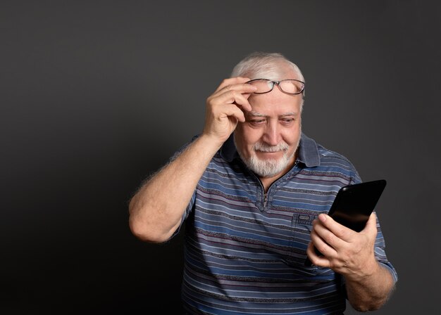 Good-natured smiling man holding glasses and looking at the tablet