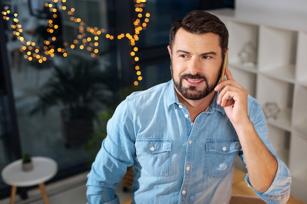 Good news. Cheerful positive handsome man talking on the phone and smiling while receiving good news