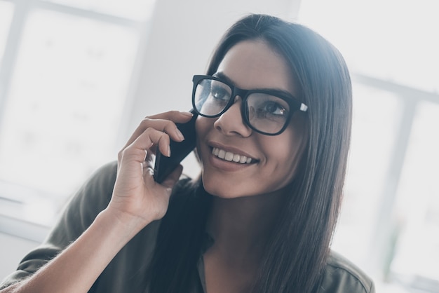 Good news! Confident young woman in smart casual wear talking on the mobile phone and smiling