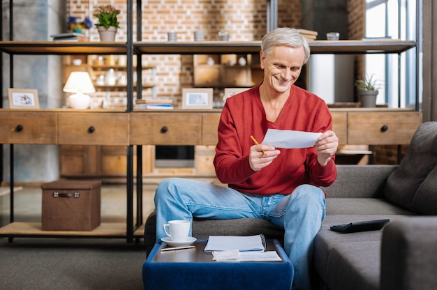 Photo good news. delighted positive joyful man looking at the note and smiling while receiving good news