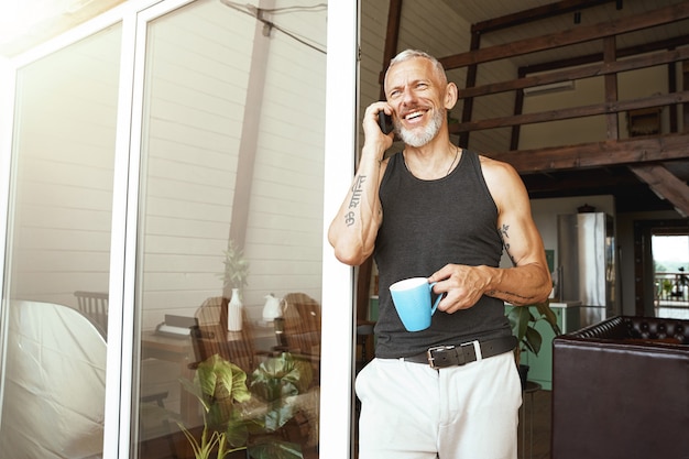 Good news happy middle aged caucasian man talking by mobile phone while drinking coffee near