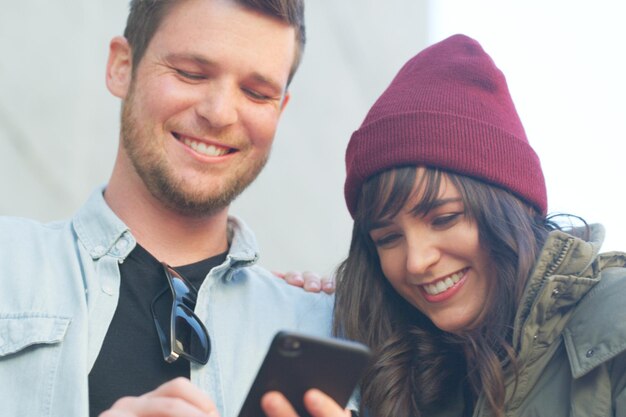 Фото Хорошие новости всегда оставят улыбку на вашем лице обрезанный снимок нежной молодой пары, которая вместе разговаривает по мобильному телефону на открытом воздухе