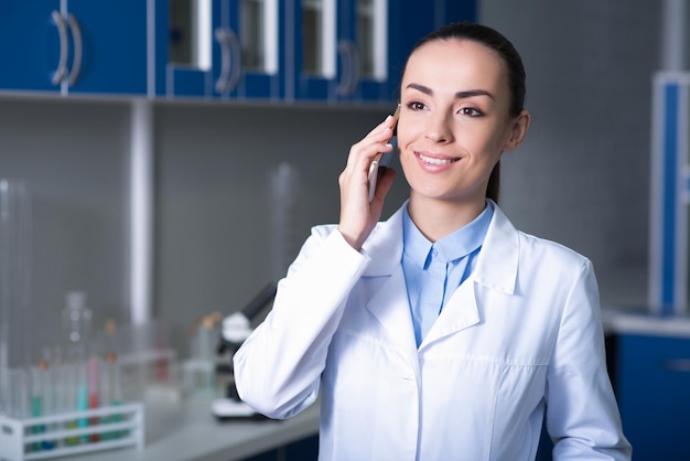 Good news Young nicelooking cute scientist standing in the lab talking by cellphone and smiling