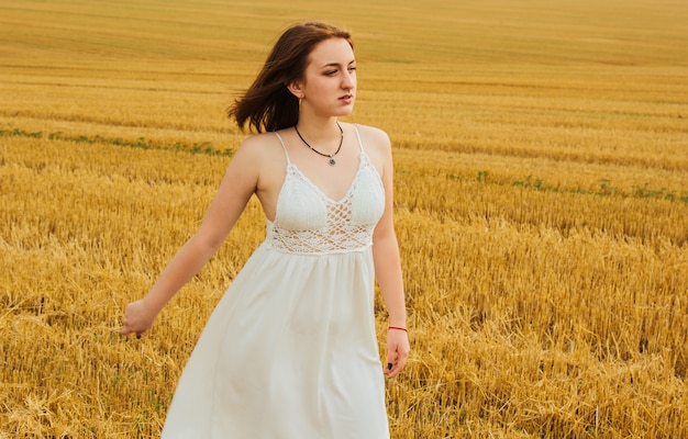 Good outdoor recreation. Young beautiful redhead woman in the middle of a wheat field, having fun. Summer landscape, good weather. Windy day with the sun and clouds. White cotton dress, eco style.