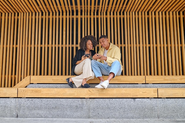 Good photo. African american inspired guy showing photo in camera to interested girlfriend sitting chatting outdoors