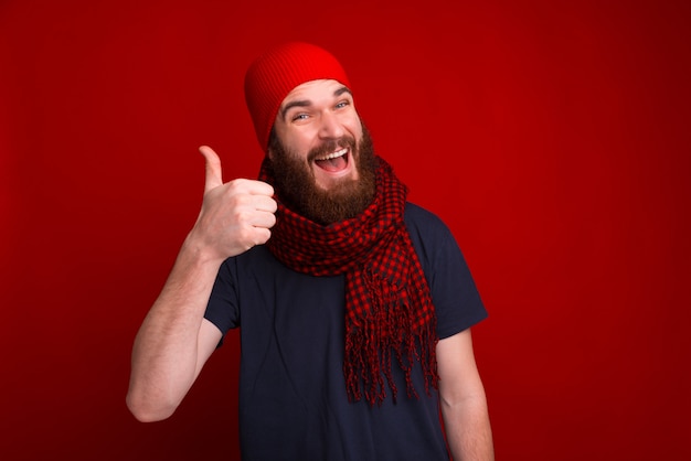 GOOD !!! Photo of bearded guy showing thumb at camer and wearing red hat and scarf