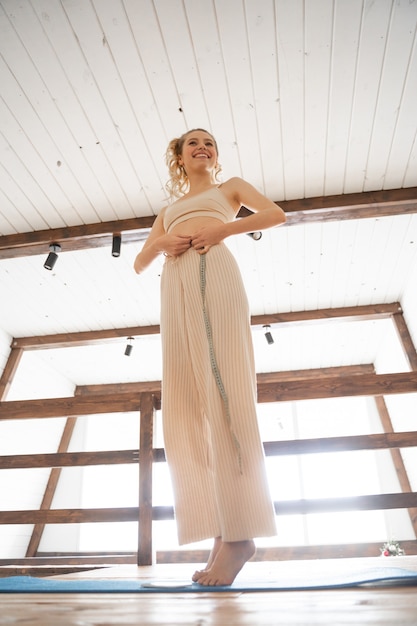 Good results. Pleased young woman keeping smile on her face, standing on yoga mat