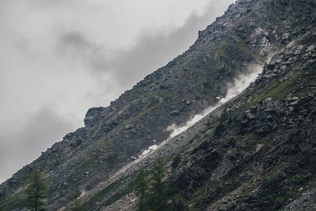 Premium Photo  Good shot of rockfall on rocky mountain steep slope and  long trail of dust. good moment of dangerous scene with falling stones and  boulder from rocks. rockfall in mountains.