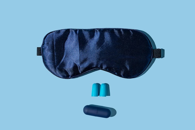 Good sleep concept blue sleeping mask and earplugs with\
individual capsule container on blue background