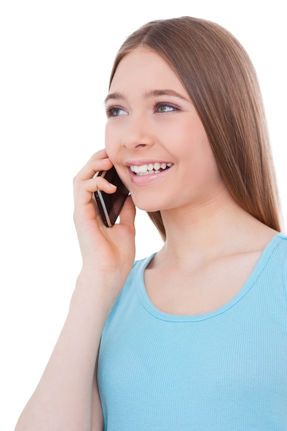 Хорошая беседа. веселая девочка-подросток разговаривает по мобильному телефону и улыбается, стоя изолированной на белом