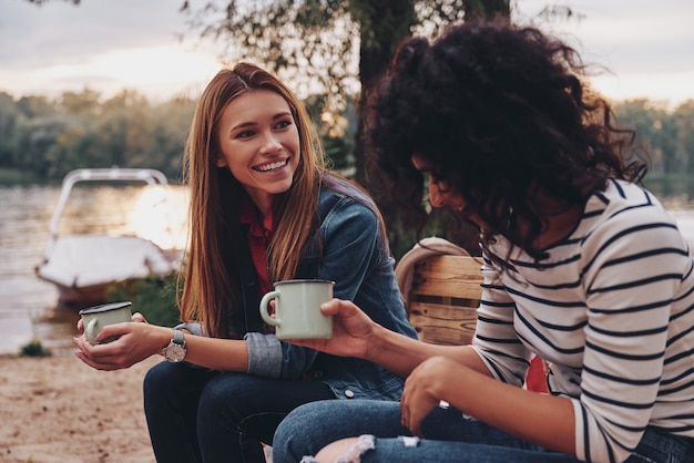 Photo good talk with friend. two young beautiful women in casual wear smiling and talking while enjoying camping near the lake