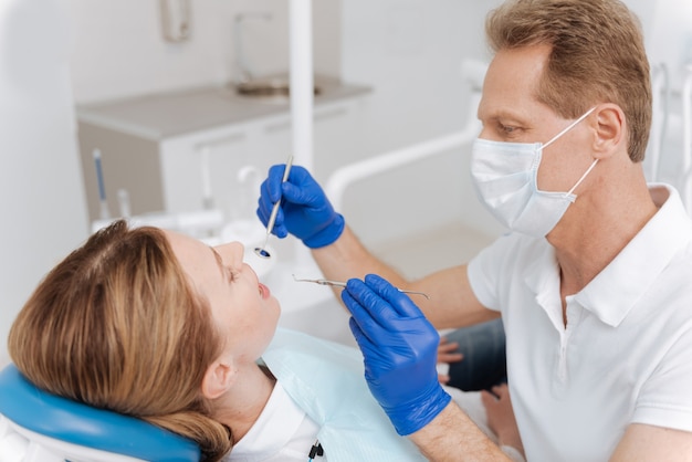 Good trained excellent doctor employing specialized medical equipment for examining patients teeth and figuring out the diagnosis
