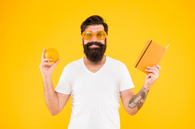 A good weight loss book bearded man holding book and orange fruit on yellow background hipster reading diet book keeping the book in home library