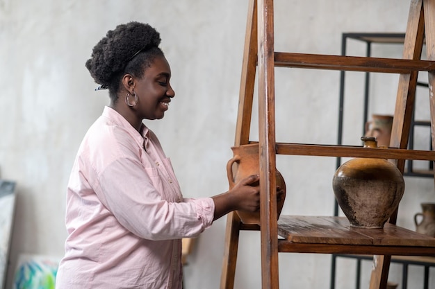 Bella donna africana in piedi vicino agli scaffali con ceramiche