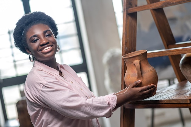 Goodlooking african woman standing near the shelves with ceramics