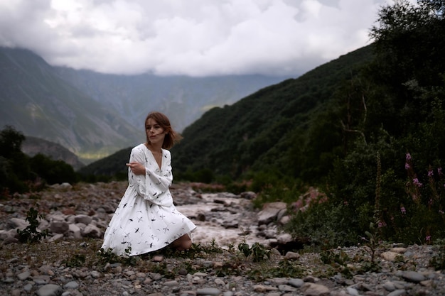 Goodlooking woman in a white dress is sitting on the ground Incredible landscape of mountains