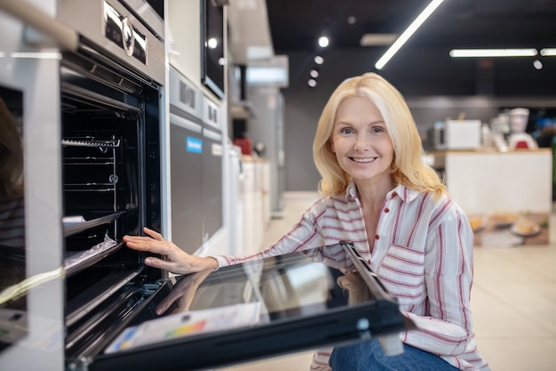 Foto merci per la casa. cliente biondo scegliendo forno in uno showroom e sorridente