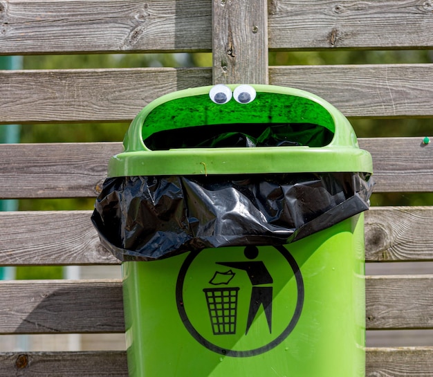 Googly eyes on a green trash can mounted on a wooden fence