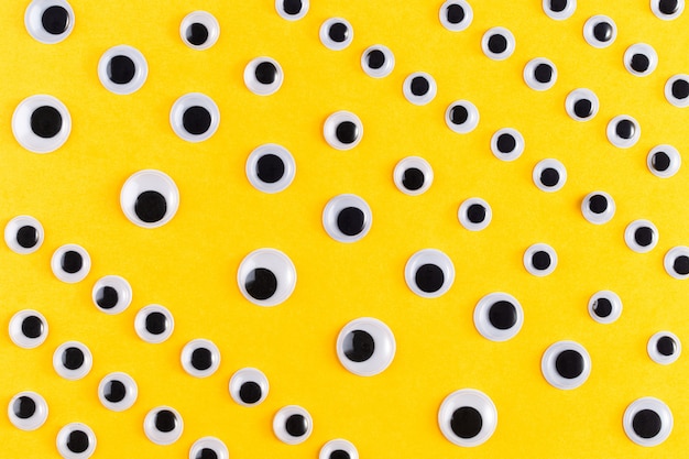 Googly plastic eyes pattern on yellow backgroud. Flat lay