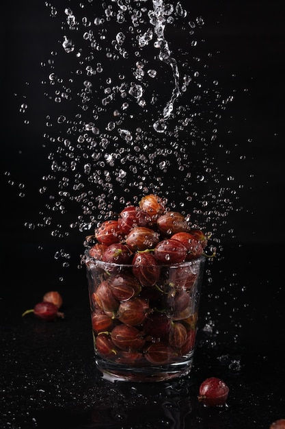 gooseberries in a glass with water drops, dark background, splash,