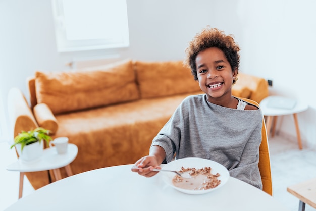 Gorgeous african american little girl eating cereals, looking at camera.