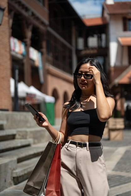 Gorgeous Asian woman enjoys shopping in the city walking while holding her phone and shopping bags