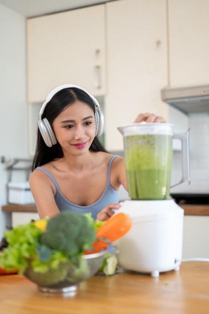 Foto una splendida donna asiatica in abbigliamento sportivo sta preparando il suo sano frullato verde disintossicante in cucina