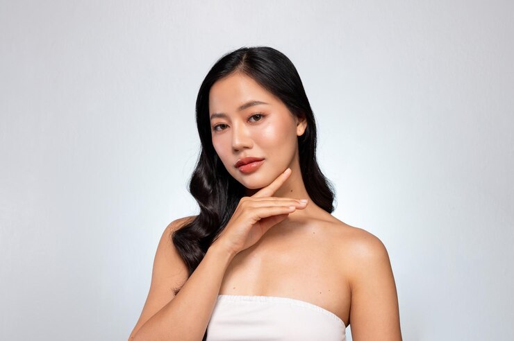 Photo gorgeous asian woman with a beautiful face poses against a grey background gently touching her chin