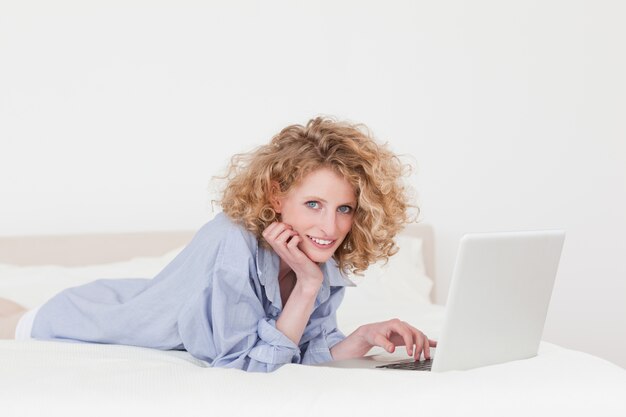 Красивая блондинка женщина, расслабляющий с ее ноутбуком, лежа на кровати