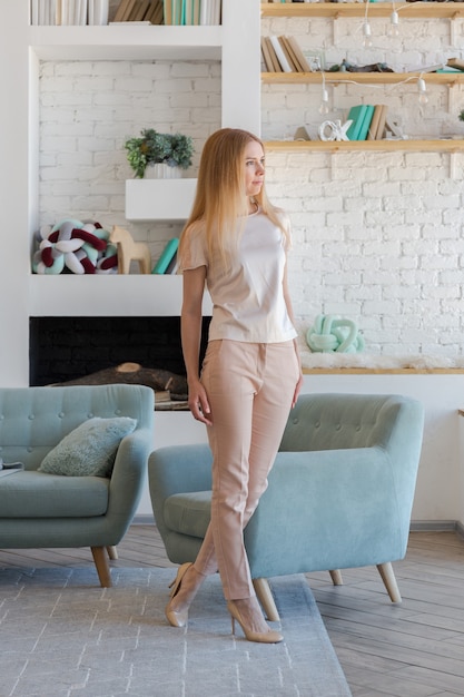 Gorgeous blonde lady in fashionable spacious apartment with a stylish design in green, grey and white pastel colors with big window and decorative walls