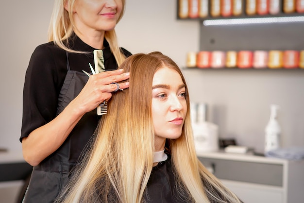 Gorgeous blonde long hair woman and her hairdresser looking and checking out hairstyle. Beautiful hairstyle of a young blonde woman after dying hair in a beauty salon, results of hair treatment.